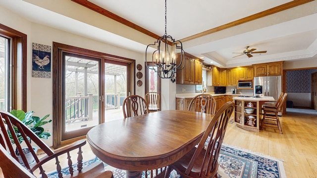 dining room with crown molding, ceiling fan with notable chandelier, a raised ceiling, and light wood-style floors