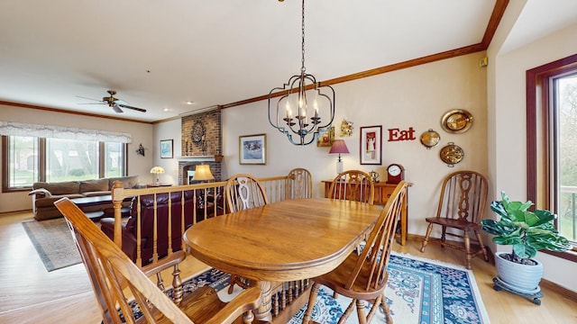 dining area featuring crown molding, a fireplace, light wood-type flooring, baseboards, and ceiling fan with notable chandelier