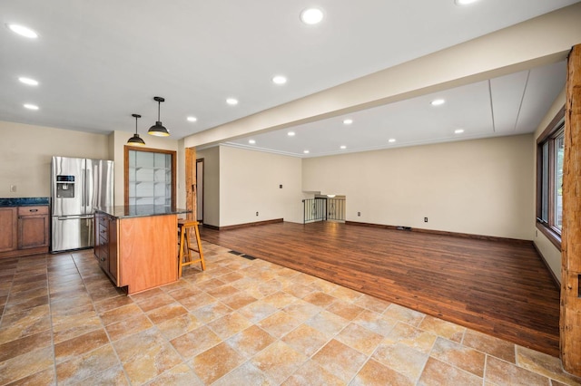 kitchen featuring stainless steel refrigerator with ice dispenser, a kitchen breakfast bar, baseboards, stone tile floors, and a center island