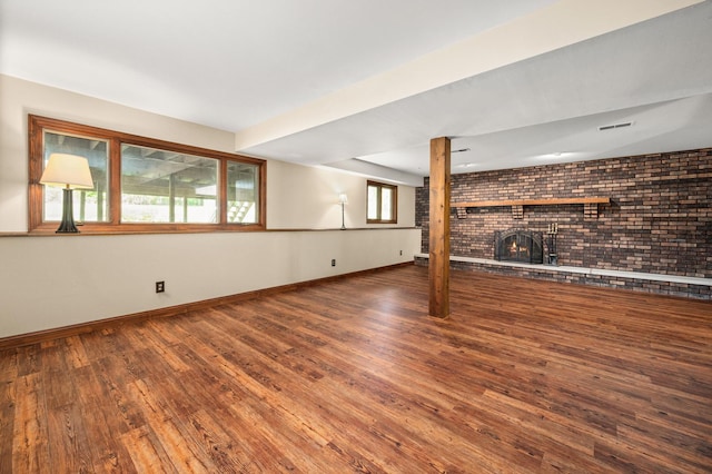 unfurnished living room featuring brick wall, baseboards, a brick fireplace, and wood finished floors