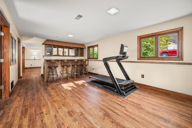 exercise room with wood finished floors, bar area, plenty of natural light, and baseboards