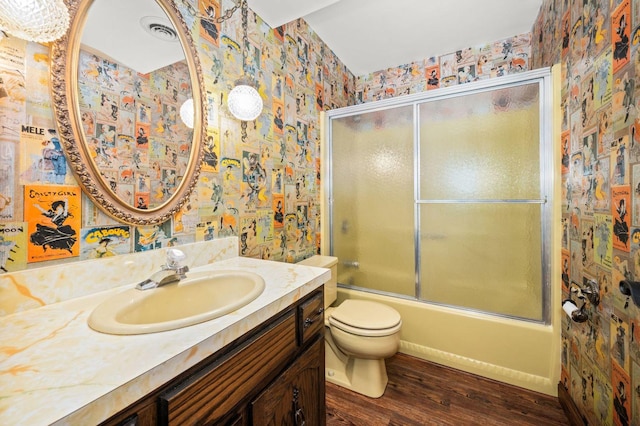 bathroom featuring wallpapered walls, wood finished floors, vanity, toilet, and shower / bath combination with glass door