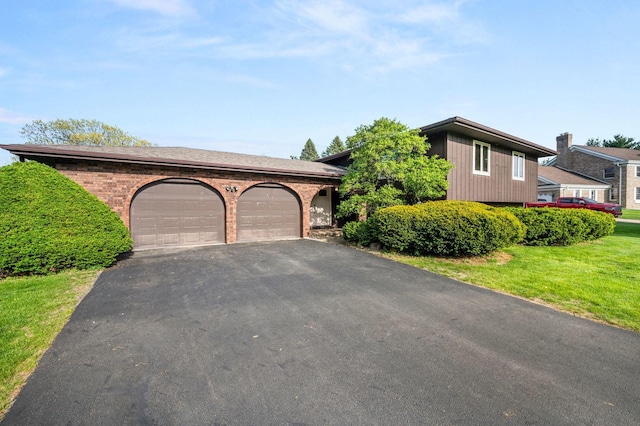 view of front of house with a garage, asphalt driveway, brick siding, and a front yard