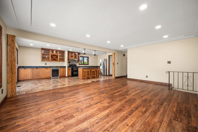 unfurnished living room featuring dark wood-type flooring, beverage cooler, recessed lighting, bar area, and baseboards