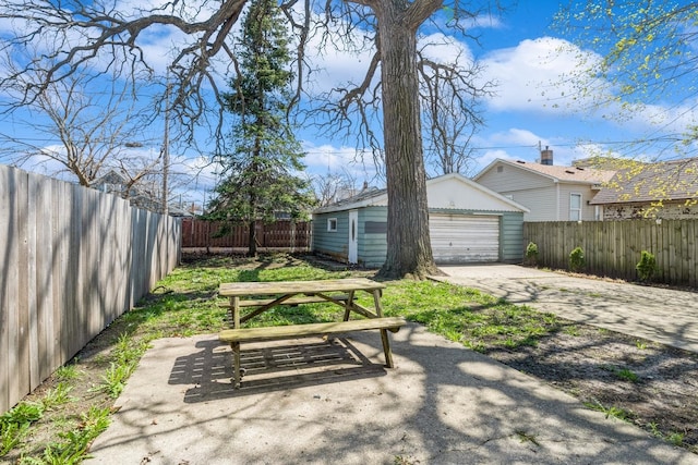 view of yard featuring a detached garage, a fenced backyard, an outbuilding, and concrete driveway