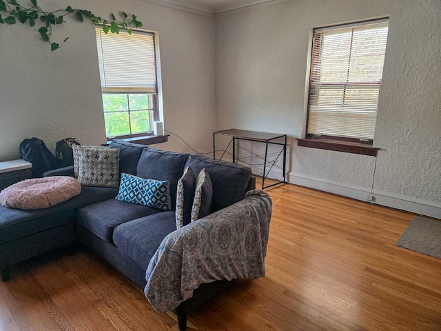 living area featuring ornamental molding, a textured wall, baseboards, and wood finished floors