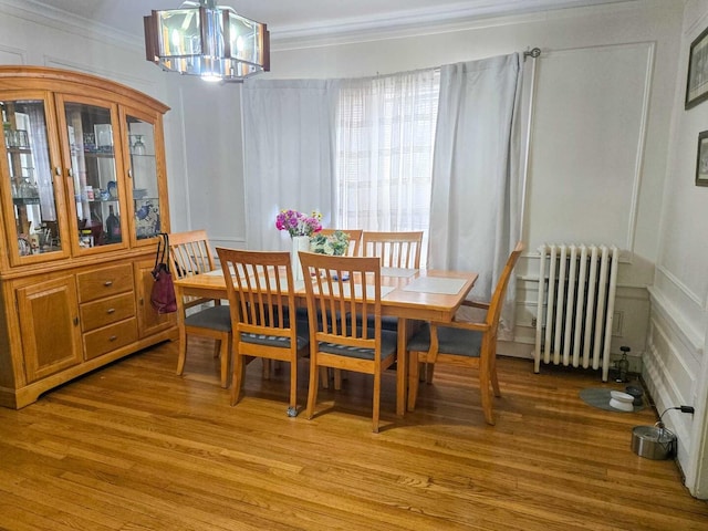 dining area featuring radiator, light wood finished floors, a decorative wall, and crown molding