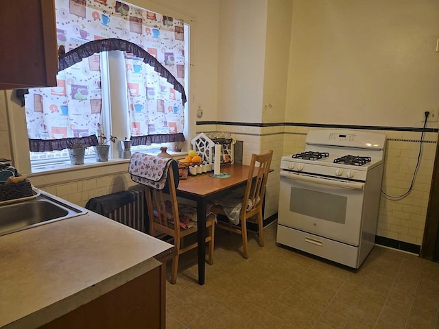 kitchen featuring wainscoting, tile walls, tile patterned floors, and white gas stove