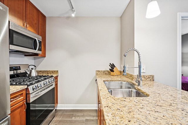 kitchen featuring stainless steel appliances, a sink, baseboards, light stone countertops, and rail lighting