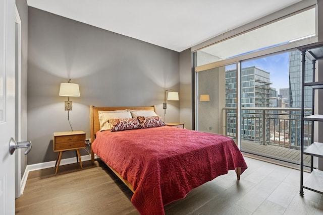 bedroom with access to outside, wood finished floors, a view of city, a wall of windows, and baseboards