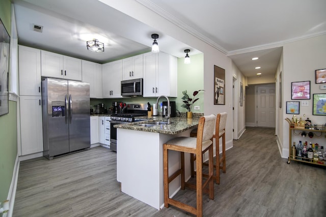 kitchen with crown molding, dark stone countertops, a sink, stainless steel appliances, and a peninsula