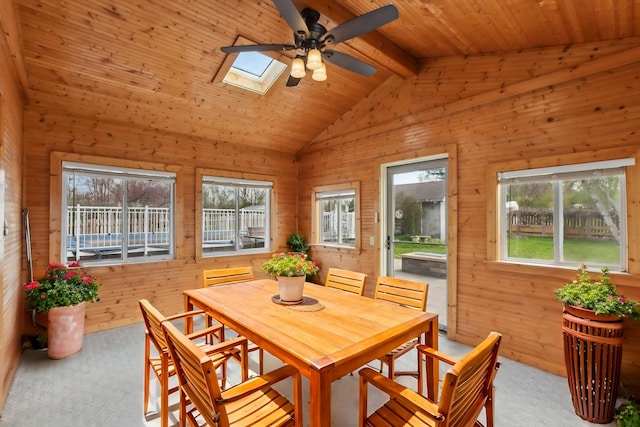 carpeted dining room featuring wooden walls, ceiling fan, plenty of natural light, and vaulted ceiling with skylight