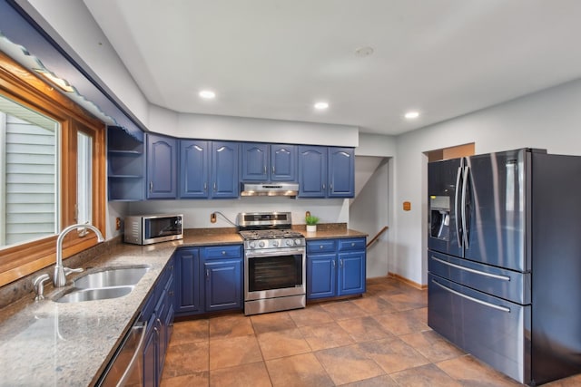 kitchen featuring a sink, appliances with stainless steel finishes, under cabinet range hood, blue cabinetry, and stone counters