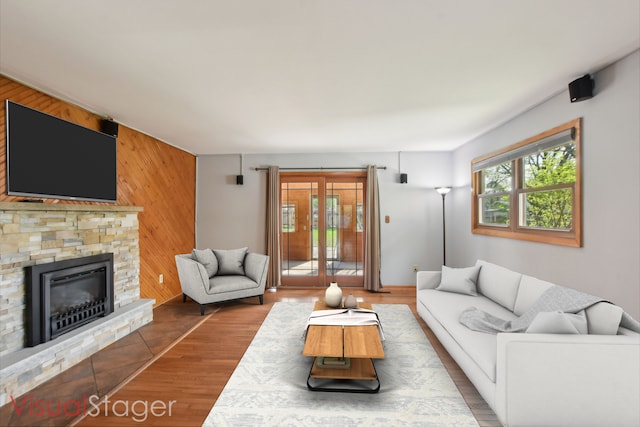 living room featuring wood walls, wood finished floors, and a stone fireplace