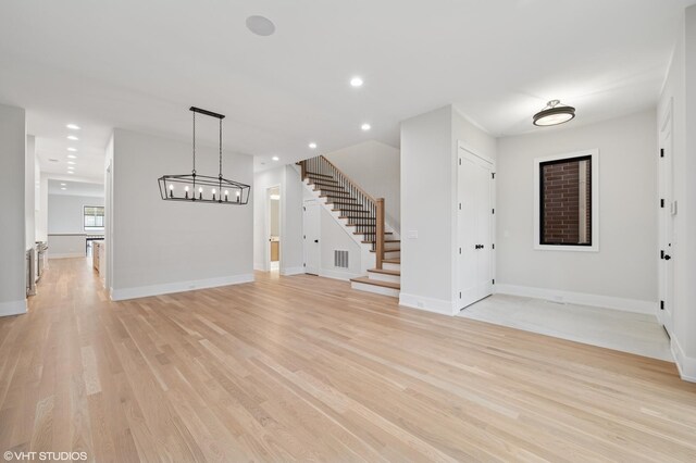unfurnished living room with baseboards, stairs, visible vents, and light wood-style flooring