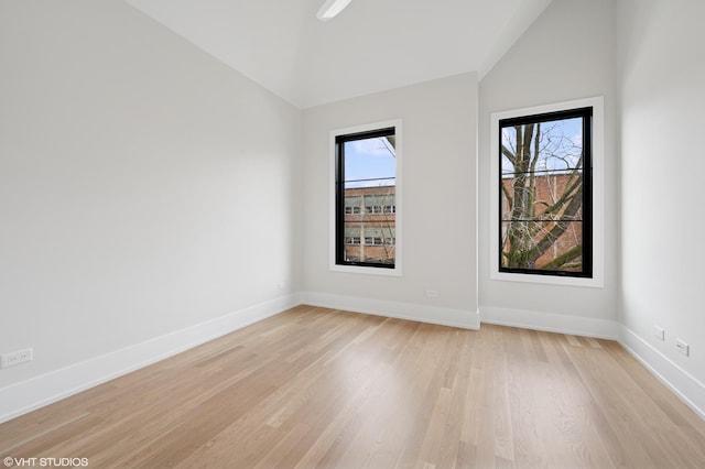 spare room featuring vaulted ceiling, baseboards, and light wood-style flooring