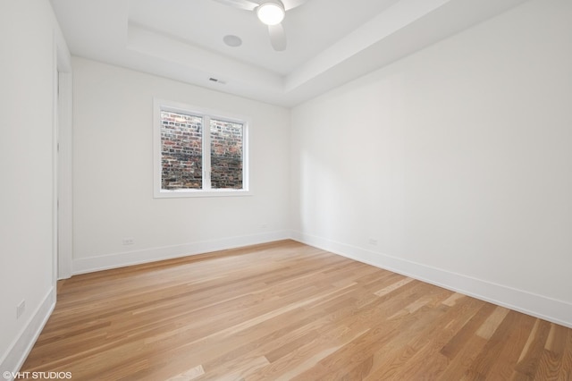 spare room with light wood-type flooring, baseboards, a ceiling fan, and a tray ceiling