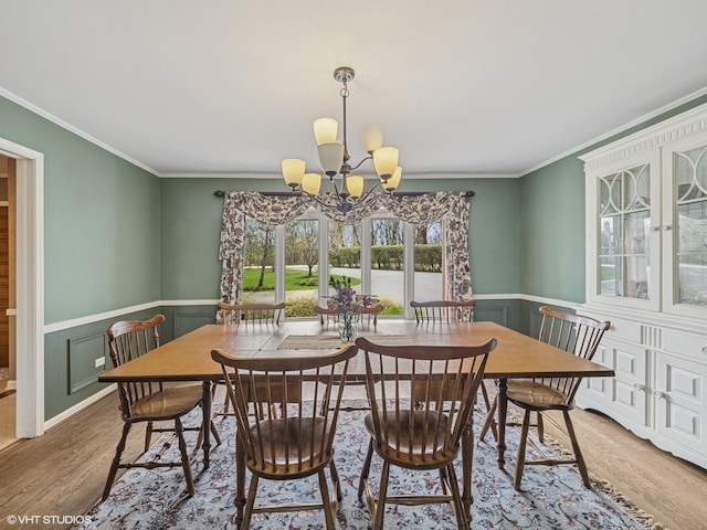 dining space featuring a notable chandelier, wainscoting, a decorative wall, wood finished floors, and ornamental molding