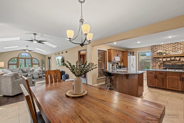 dining space featuring light tile patterned floors, a skylight, plenty of natural light, a ceiling fan, and vaulted ceiling