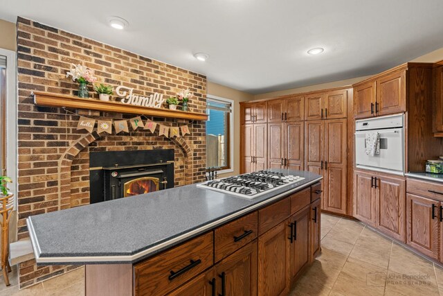 kitchen with oven, stainless steel gas cooktop, dark countertops, and a brick fireplace