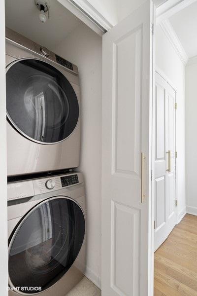 laundry area with laundry area, ornamental molding, wood finished floors, stacked washer / dryer, and baseboards