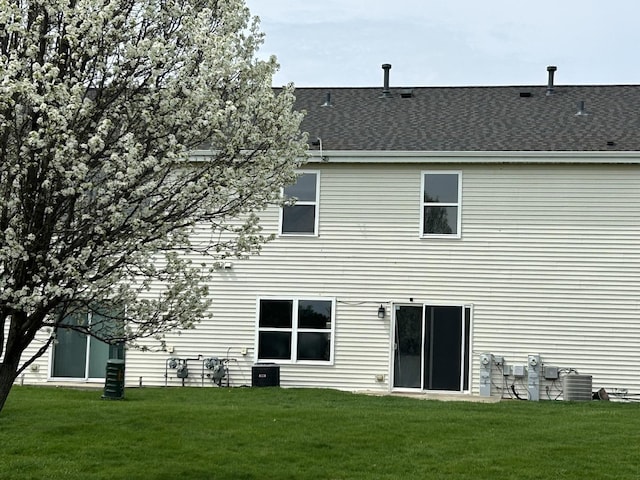back of house with a yard, central AC unit, and a shingled roof
