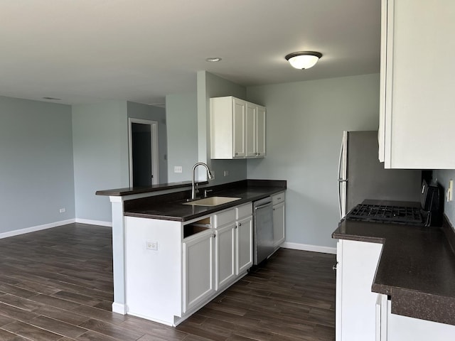 kitchen with a peninsula, dark countertops, baseboards, a sink, and stainless steel appliances