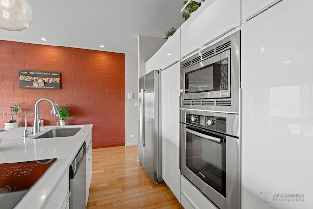 kitchen with recessed lighting, light wood finished floors, stainless steel appliances, a sink, and white cabinetry