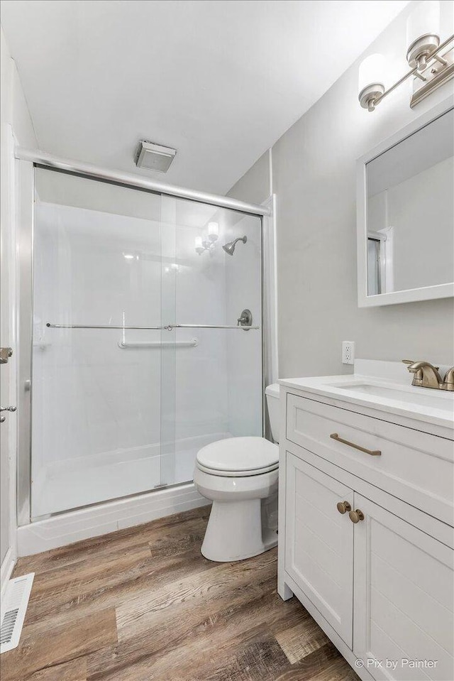 bathroom featuring vanity, visible vents, wood finished floors, toilet, and a shower stall