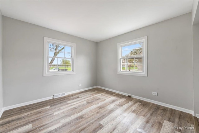 empty room featuring baseboards, visible vents, plenty of natural light, and light wood-type flooring