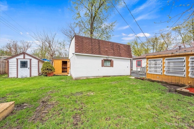 back of house featuring a lawn, a shingled roof, an outbuilding, and a shed