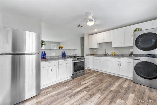 kitchen with stacked washer / drying machine, light stone countertops, stainless steel appliances, a ceiling fan, and white cabinetry
