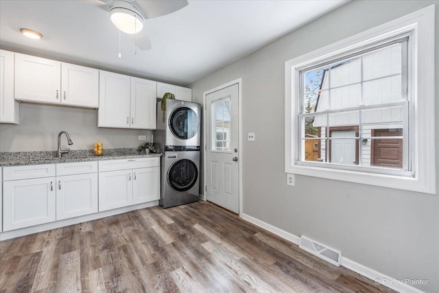 laundry area featuring cabinet space, a sink, stacked washing maching and dryer, baseboards, and visible vents
