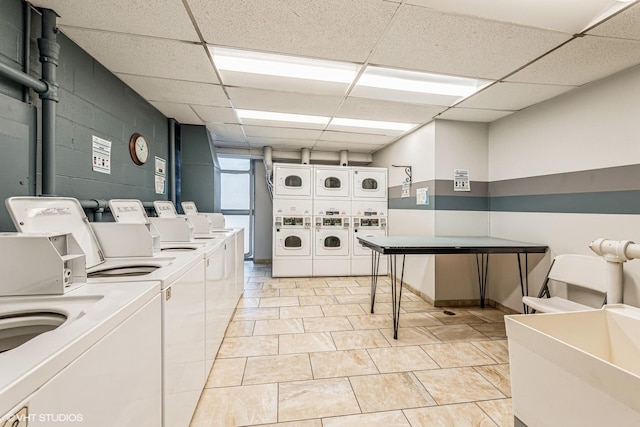 community laundry room featuring concrete block wall, separate washer and dryer, light tile patterned floors, and stacked washer and clothes dryer