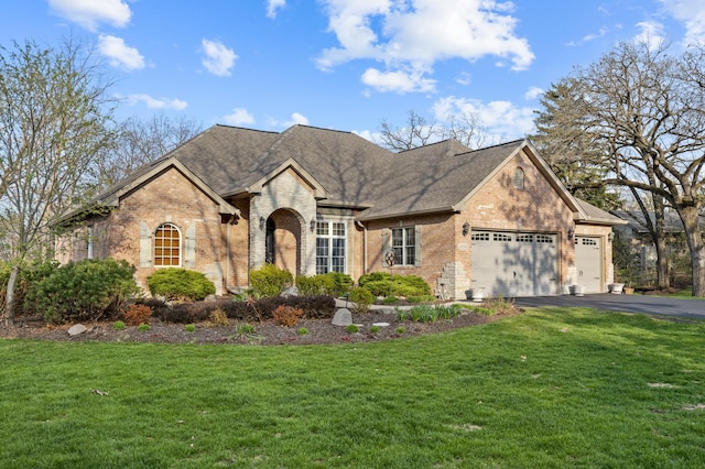 french country home featuring aphalt driveway, a front lawn, an attached garage, and brick siding