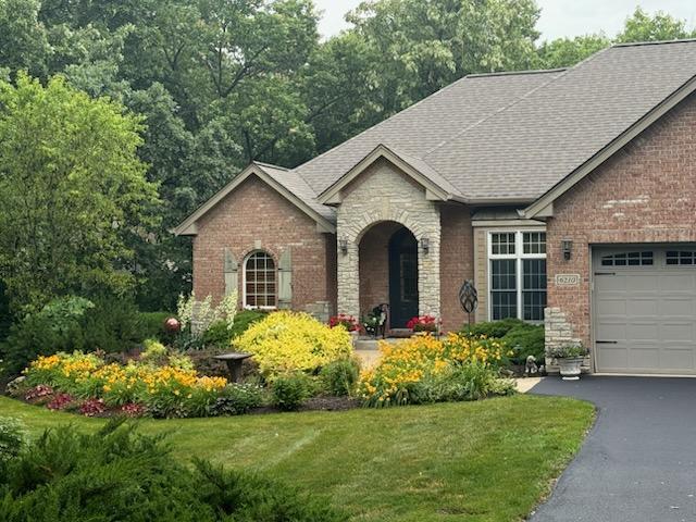 view of front of property with stone siding, roof with shingles, an attached garage, brick siding, and a front lawn