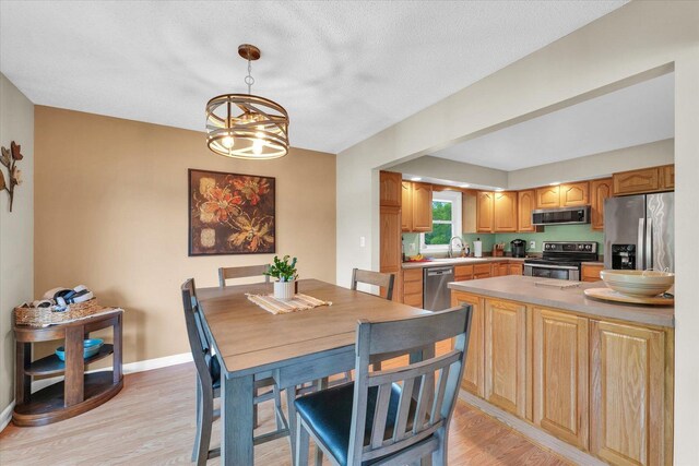 dining space featuring baseboards, light wood-type flooring, a textured ceiling, and a notable chandelier