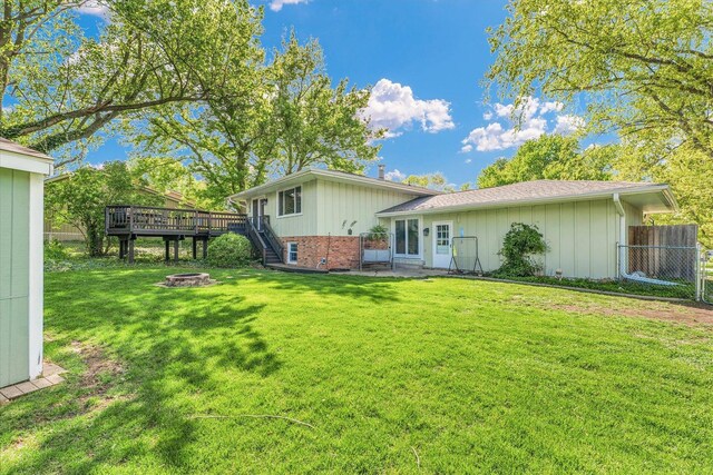 rear view of house featuring fence, a deck, board and batten siding, an outdoor fire pit, and a yard
