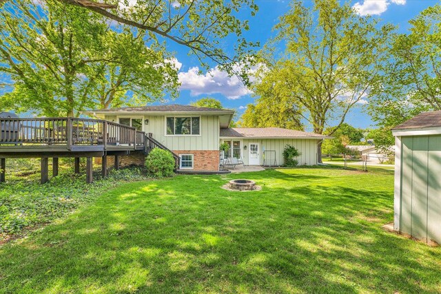 rear view of property with board and batten siding, a lawn, a deck, brick siding, and an outdoor fire pit