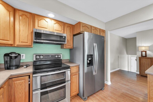 kitchen featuring baseboards, light countertops, light wood-style flooring, and appliances with stainless steel finishes