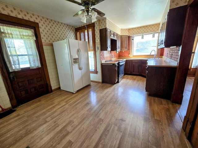 kitchen with white refrigerator with ice dispenser, wallpapered walls, ceiling fan, light countertops, and electric range