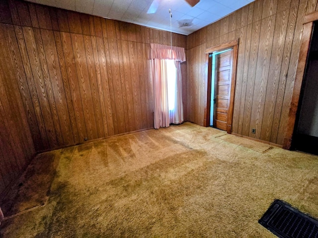 carpeted spare room featuring wood walls and a ceiling fan