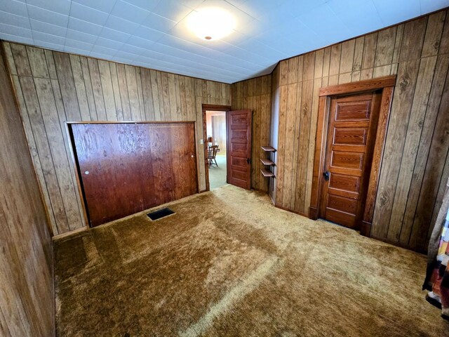carpeted empty room featuring wooden walls and visible vents
