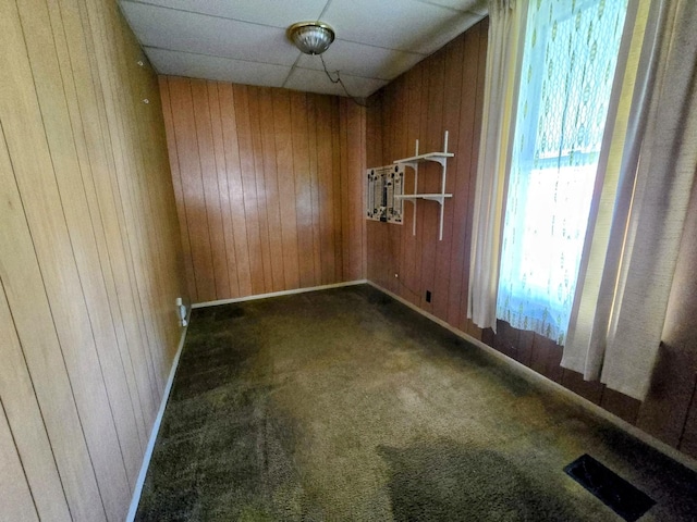 empty room featuring wooden walls, baseboards, visible vents, and carpet