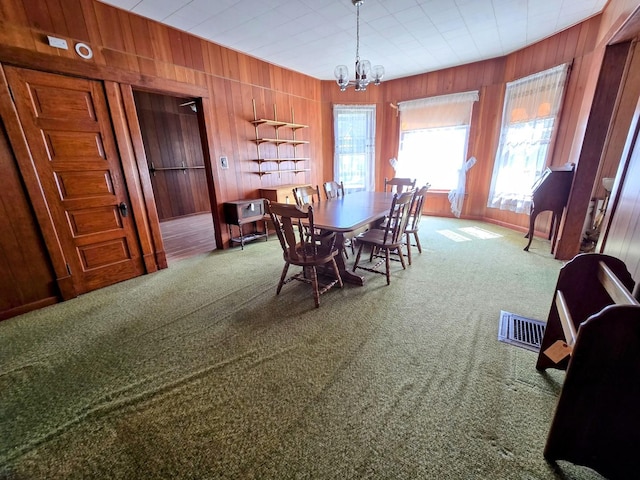 dining area featuring visible vents, wood walls, carpet, and a chandelier