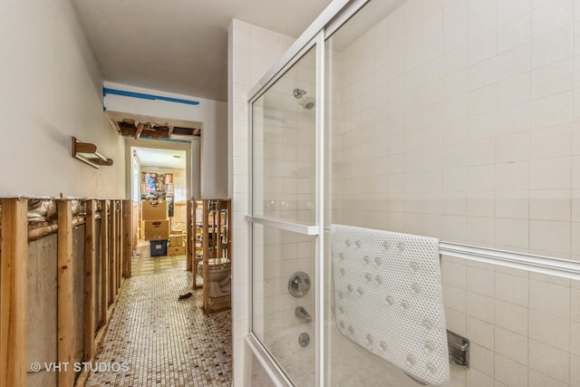 bathroom with tile patterned flooring, tile walls, and bath / shower combo with glass door
