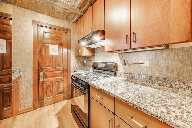 1312 N Astor St, Chicago, IL 60610 - kitchen with black gas range oven, under cabinet range hood, backsplash, light wood finished floors, and light stone counters