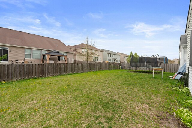 view of yard featuring a gazebo, a fenced backyard, a trampoline, and a residential view