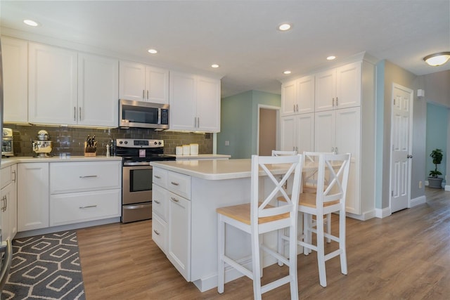 kitchen with appliances with stainless steel finishes, tasteful backsplash, light wood-type flooring, light countertops, and white cabinetry