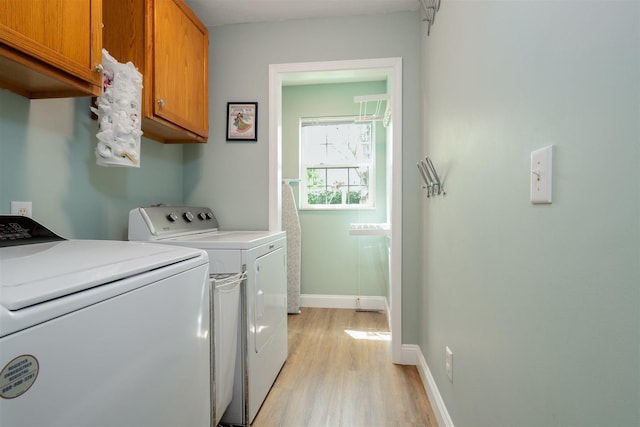 clothes washing area with baseboards, cabinet space, light wood finished floors, and washer and dryer